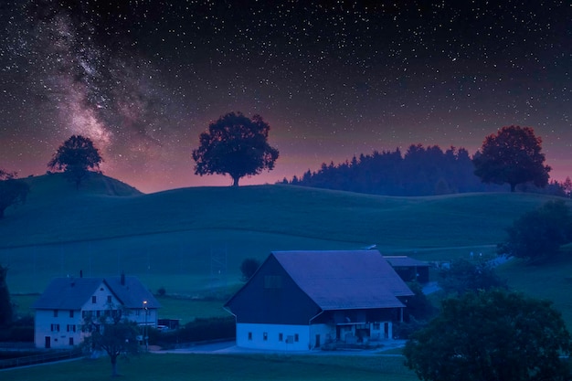un cielo nocturno estrellado sobre una granja con un árbol en primer plano