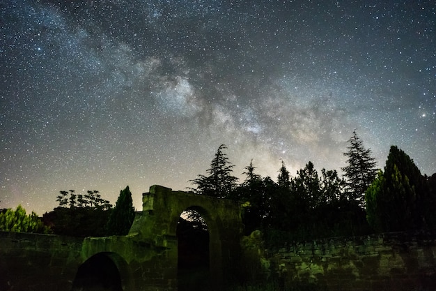 Cielo nocturno con la Vía Láctea sobre el bosque y las ruinas en España