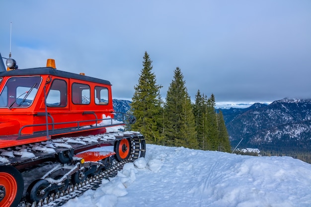 Cielo nublado sobre picos nevados. Laderas boscosas. Snowcat rojo en primer plano