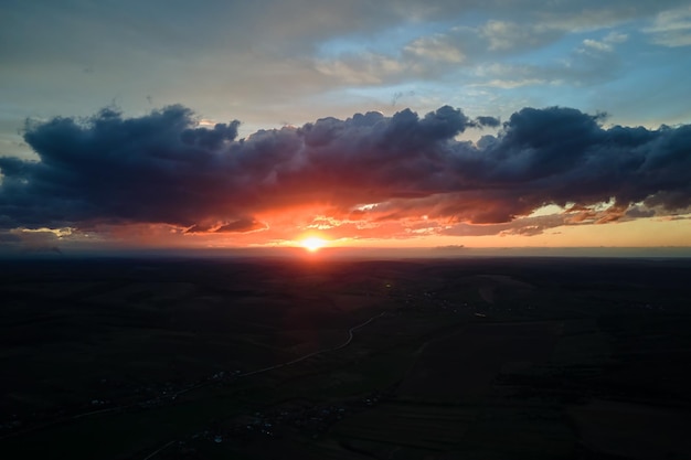 Cielo de puesta de sol colorido brillante con puesta de sol y nubes vibrantes sobre paisaje oscuro