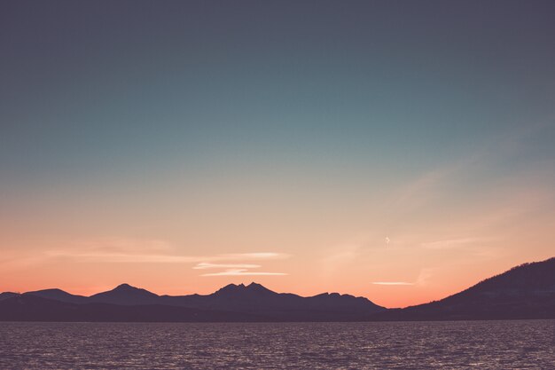 Foto cielo rosado hermoso de la puesta del sol sobre el silhourtte de las montañas en la playa.