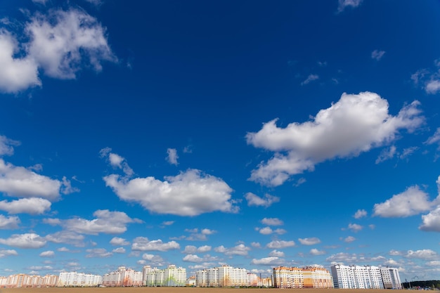 Cielos azules profundos con fondo de nubes blancas y zona residencial moderna de varios pisos en el horizonte