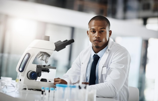 Ciência de confiança e retrato de homem negro com microscópio estudo médico e pesquisa saúde biotecnológica e cientista sério em laboratório para o desenvolvimento farmacêutico estágio e orgulho