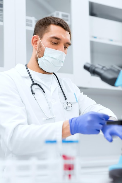 ciência, medicina, tecnologia, segurança e conceito de pessoas - jovem cientista masculino usando luvas de proteção em laboratório médico