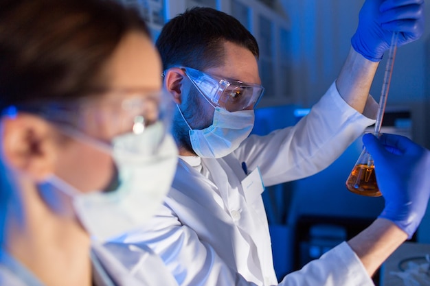 ciência, química, biologia, medicina e conceito de pessoas - close-up de jovens cientistas com pipeta e frascos fazendo teste ou pesquisa em laboratório clínico