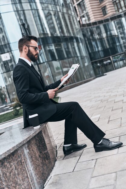 Ciente das últimas notícias. Jovem bonito de terno completo lendo um jornal