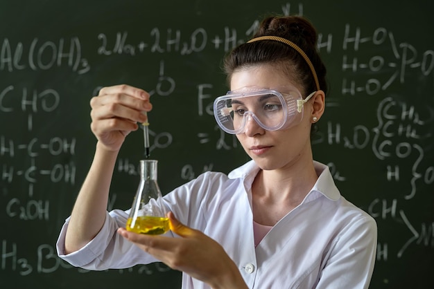 Científica haciendo pruebas científicas con matraz químico y líquido en el laboratorio escolar