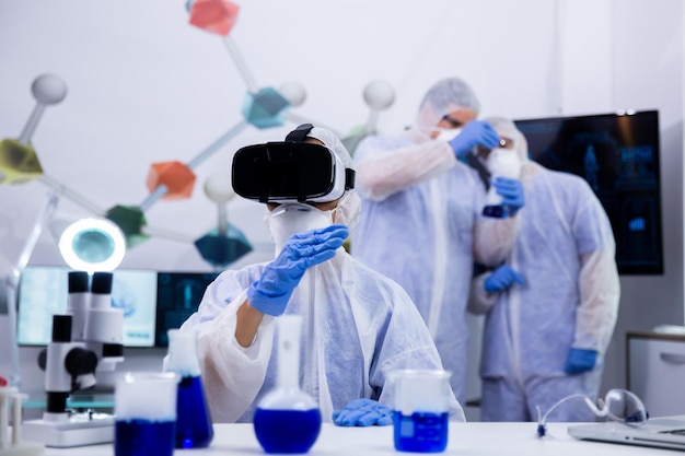 Una científica en un moderno laboratorio de investigación se desliza con gafas de realidad virtual. Fumar líquido azul en tubos de ensayo.