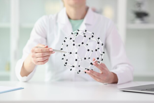 Una científica muestra un modelo de estructura molecular en sus manos sentada en una mesa de laboratorio