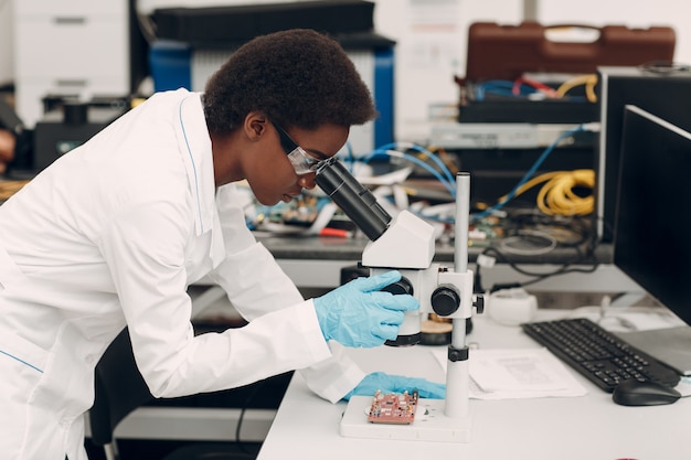 Científica mujer afroamericana que trabaja en laboratorio con instrumentos de tecnología electrónica e investigación y desarrollo de microscopios de dispositivos electrónicos por mujer negra de color