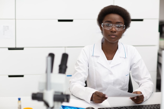 Científica mujer afroamericana que trabaja en la mesa de laboratorio con instrumentos de tecnología electrónica e investigación y desarrollo de microscopios de dispositivos electrónicos por mujer negra de color