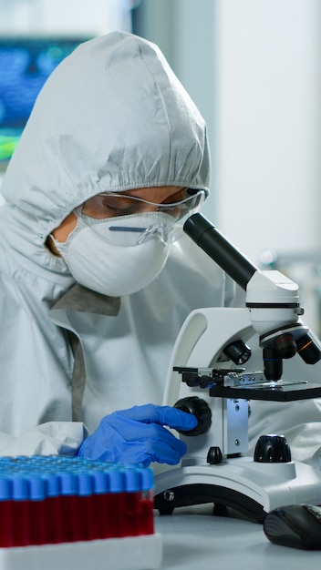 Foto científica en traje de ppe trabajando en laboratorio con microscopio moderno con portaobjetos. equipo de investigadores químicos que examinan la evolución del virus utilizando alta tecnología para la investigación científica de vacunas contra covid19