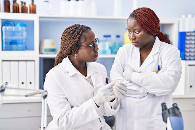 Científicas afroamericanas que buscan muestras de pie con gesto de brazos cruzados en el laboratorio