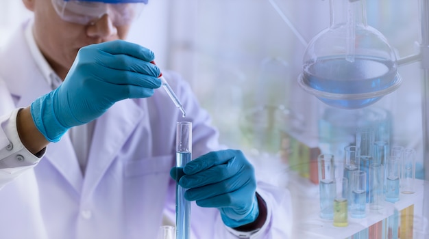 científico arrojando reactivo químico en tubo de ensayo con cristalería de laboratorio