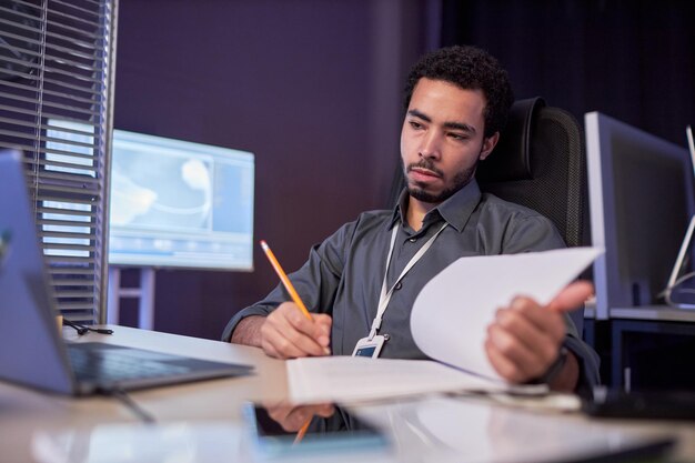 Científico de datos masculino que trabaja con documentación en el lugar de trabajo en la oficina