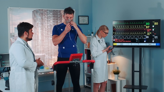 Científico del deporte de raza mixta dando instrucciones al atleta sobre cómo hacer la prueba correctamente en el laboratorio moderno con ...