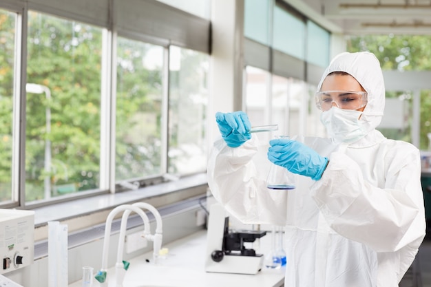 Científico femenino protegido vertiendo líquido en un matraz Erlenmeyer