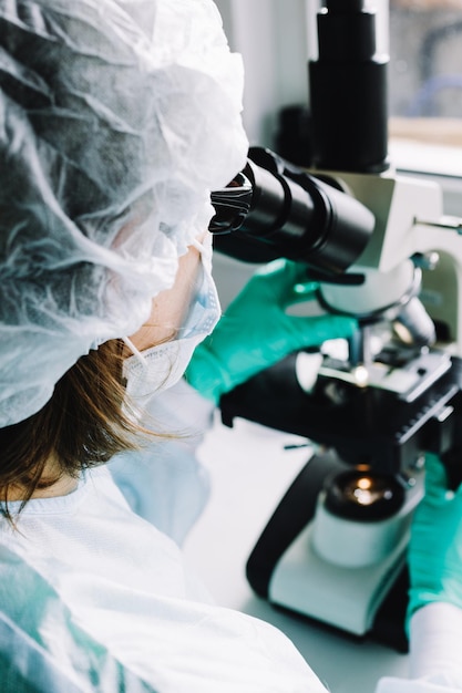 Científico en guantes médicos azules y muestras de aprendizaje uniformes con microscopio en laboratorio