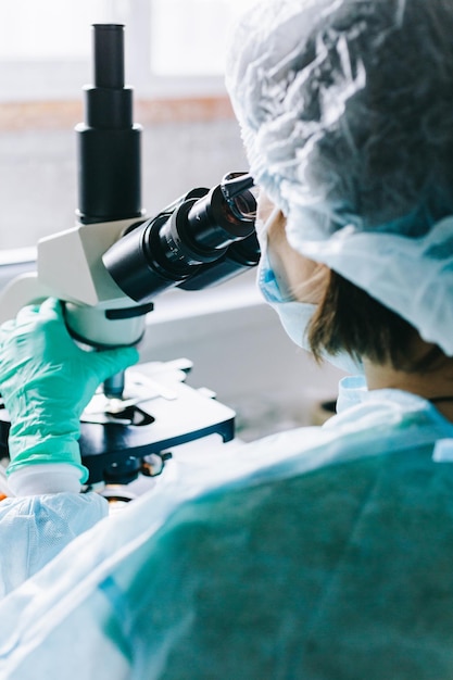 Foto científico en guantes médicos azules y muestras de aprendizaje uniformes con microscopio en laboratorio