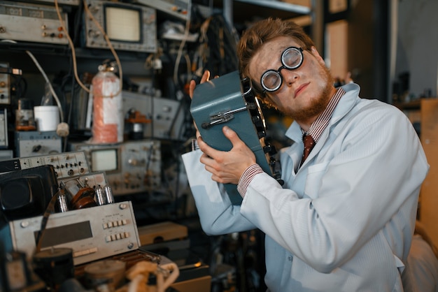 Científico loco en vasos tiene dispositivo eléctrico en laboratorio.