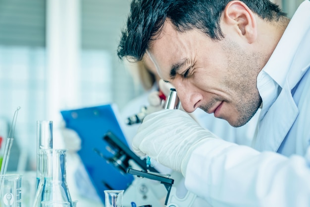 Foto científico mira al microscopio mientras realiza un examen médico en el laboratorio de ciencias