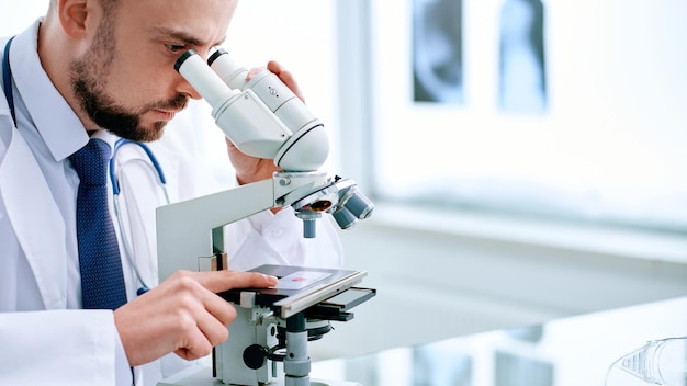 Científico mirando a través de un microscopio sentado en una mesa de laboratorio.