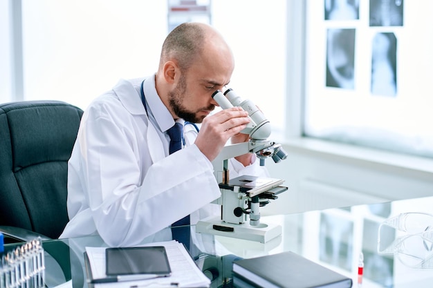 Científico mirando a través de un microscopio sentado en una mesa de laboratorio