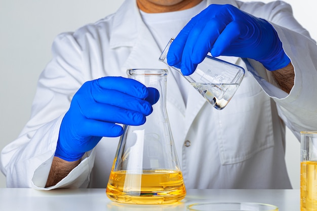 Científico o médico con guantes azules vertiendo un poco de líquido amarillo en un matraz