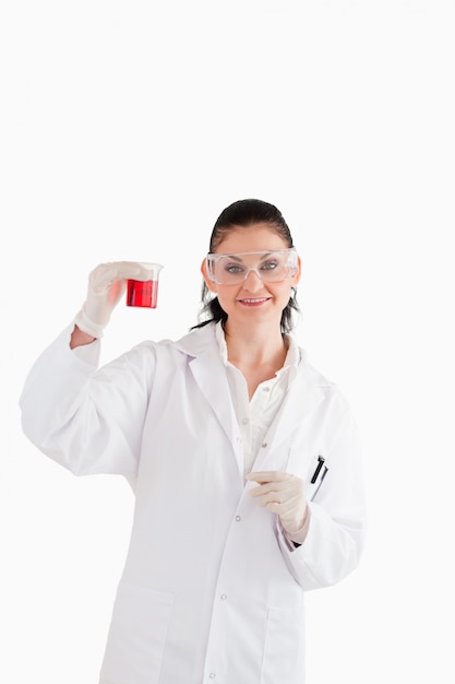 Foto científico de pelo oscuro mirando a la cámara mientras sostiene un vaso de precipitados rojo