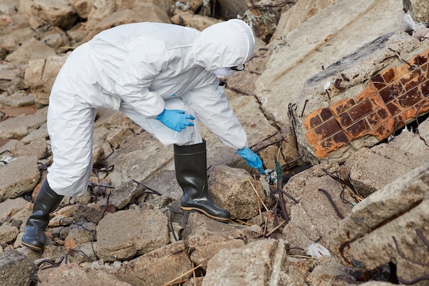 Foto científico en ropa de trabajo protectora de pie sobre las rocas y tomando muestras en un matraz al aire libre