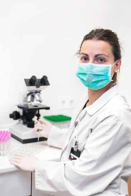 Científico de sexo femenino alegre con la máscara protectora que presenta en el laboratorio.