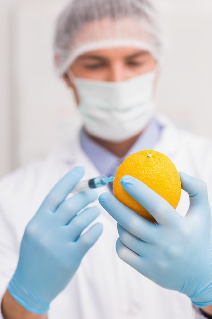 Científico sosteniendo naranja e inyectar líquido con jeringa