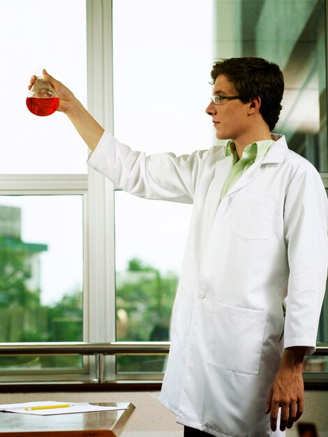 Foto científico sosteniendo un químico rojo en vasos de laboratorio