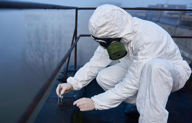 Científico trabajador con sobretodo protector y máscara de gas haciendo pruebas ecológicas en el techo