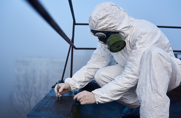 Científico trabajador con sobretodo protector y máscara de gas haciendo pruebas ecológicas en el techo