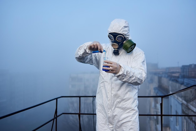 Científico trabajador con sobretodo protector y máscara de gas haciendo pruebas ecológicas en el techo