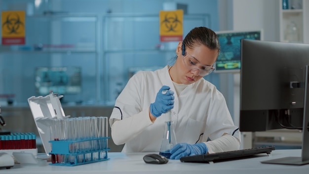 Científico trabajando con micro pipeta para líquido en vaso de precipitados y tubo de ensayo, haciendo experimentos de química en laboratorio. Investigador de bioquímica mezclando sustancias usando cuentagotas y equipo de laboratorio.