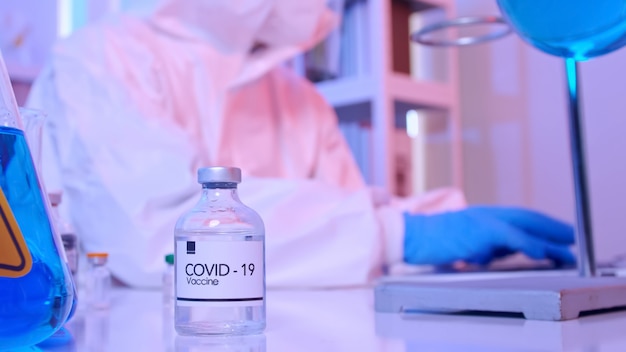 Científico con traje PPE realiza una investigación sobre la vacuna COVID 19 en un laboratorio.