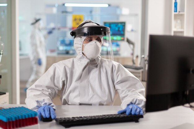 Científico vestido con traje de ppe trabajando en equipo para vacuna contra virus