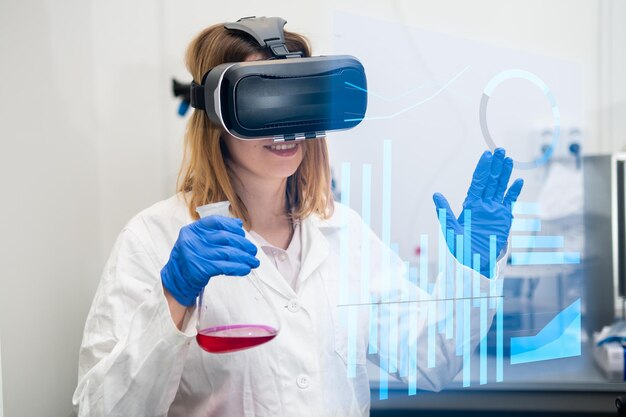 Científico en vr googles bata de laboratorio y matraz hojeando una página de interfaz virtual con gráficos