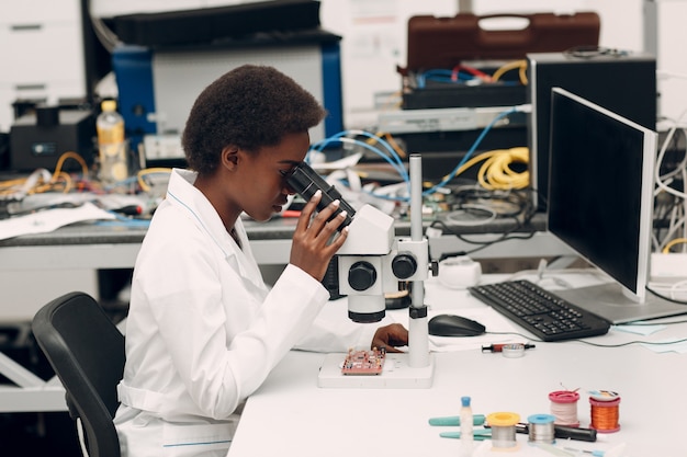 Cientista afro-americana trabalhando em laboratório com microscópio