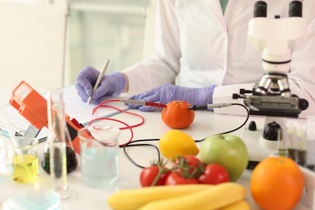 Cientista com microscópio e equipamento de pesquisa faz anotações enquanto examina muitas frutas e