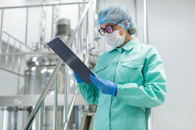 Cientista em uniforme de laboratório azul fica em escadas cromadas e olha no tanque de aço comprimido no fundo