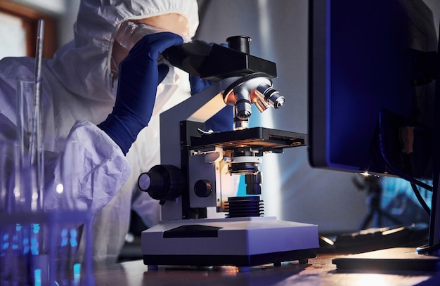 Cientista em uniforme de proteção branco trabalha com coronavírus e tubos de sangue em laboratório