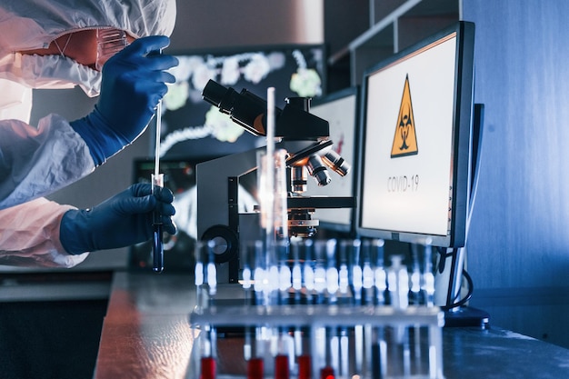 Cientista em uniforme protetor branco trabalha com coronavírus e tubos de sangue em laboratório