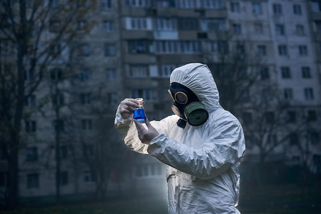 Cientista fazendo pesquisa ao ar livre usando macacão branco e máscara de gás