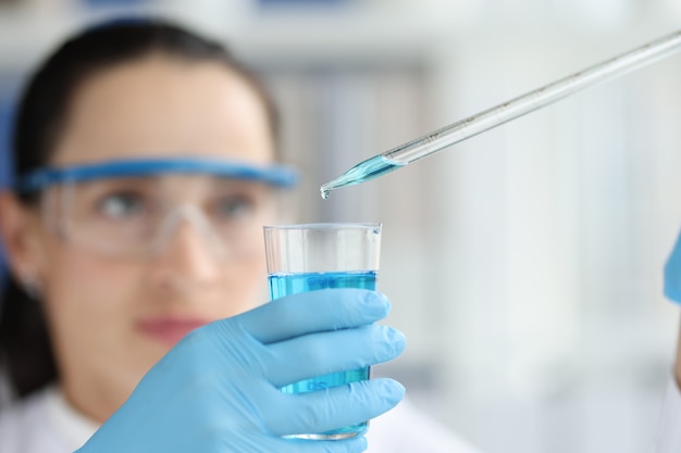 Cientista fêmea pingando e pipetando para um frasco de líquido azul na pesquisa de química doméstica em