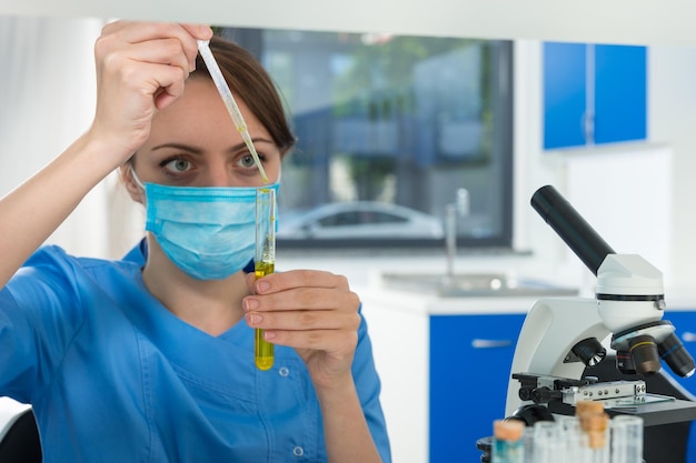 Cientista feminina concentrada em uniforme pega um líquido por pipeta de um tubo de ensaio para algumas pesquisas em um laboratório. Conceito de saúde e biotecnologia