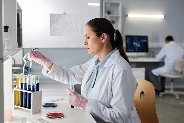 Cientista feminina de vista lateral fazendo testes na estação de trabalho em laboratório moderno