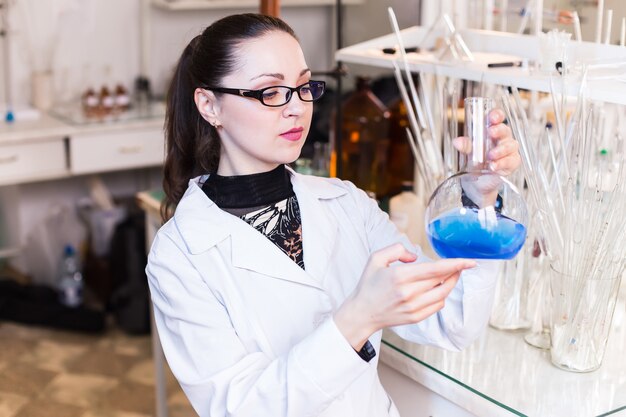 Cientista feminina em um laboratório, segurando um frasco com líquido